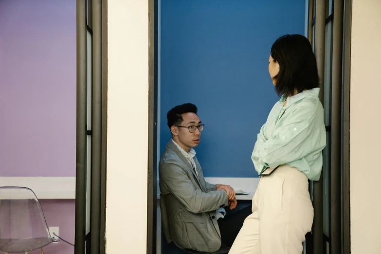 a woman standing next to a man in a room, by Jang Seung-eop, pexels contest winner, man sitting facing away, in meeting together, leaning on door, flat colour