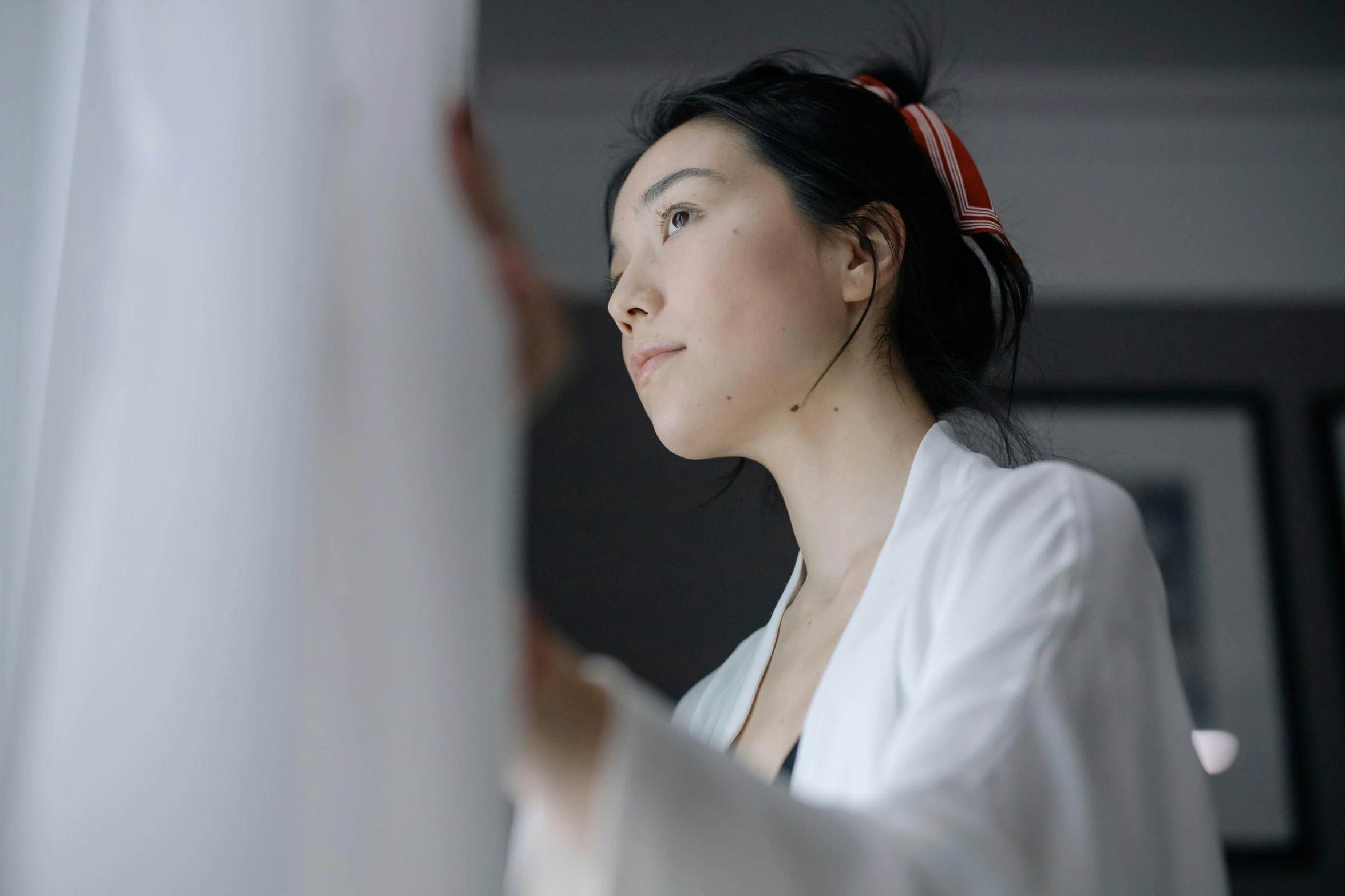 a woman in a white robe looking out a window, inspired by Qian Xuan, on a gray background, looking in mirror, low quality photo, looking upwards