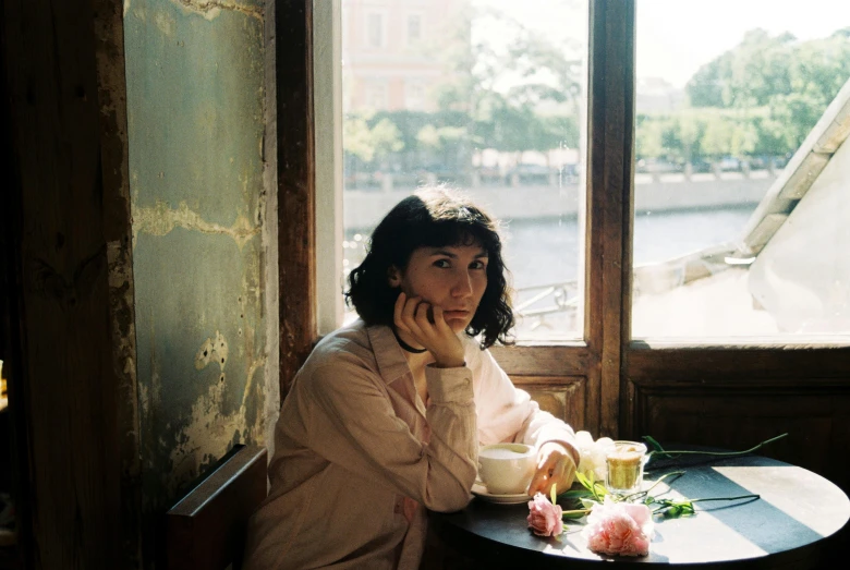 a woman sitting at a table in front of a window, by Lucia Peka, pexels contest winner, serial art, amelie poulain, sitting in a cafe, valentin serov style, shot on large format film camera