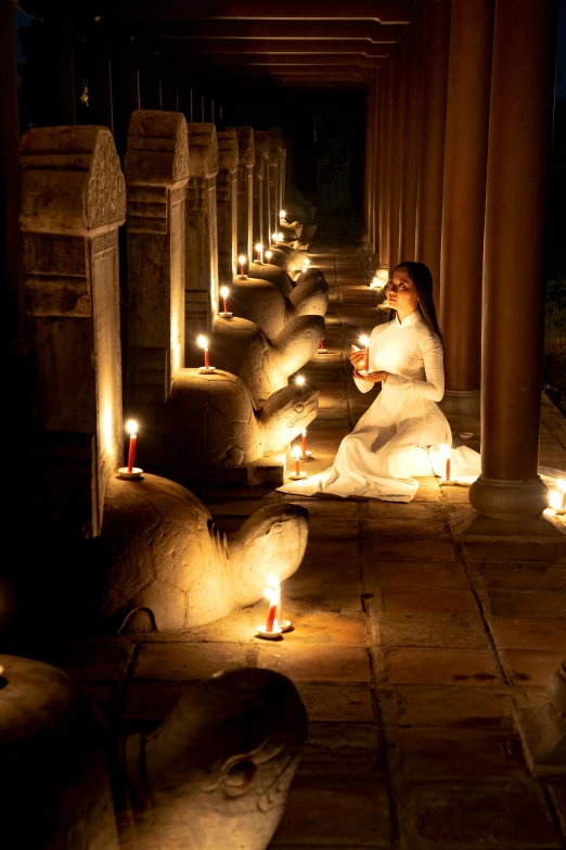 a woman sitting on the ground with candles in front of her, a statue, inspired by Steve McCurry, light and space, in an ancient vault, cambodia, serene lighting, floating lanterns