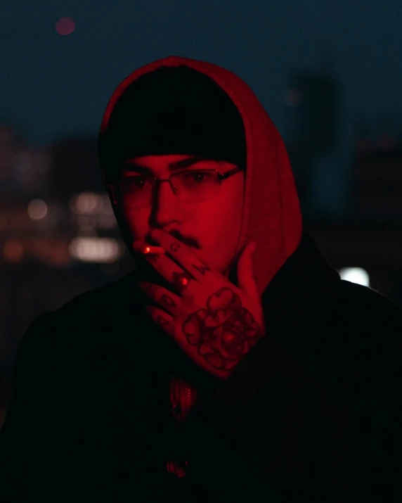 a man in a hoodie smoking a cigarette, an album cover, inspired by Elsa Bleda, trending on pexels, he has a red hat, lgbt, night view, zayn malik