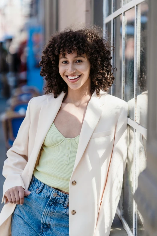 a woman with curly hair leaning against a wall, inspired by Anita Malfatti, trending on pexels, wearing a blazer, stood outside a corner shop, wearing a camisole, curly middle part haircut