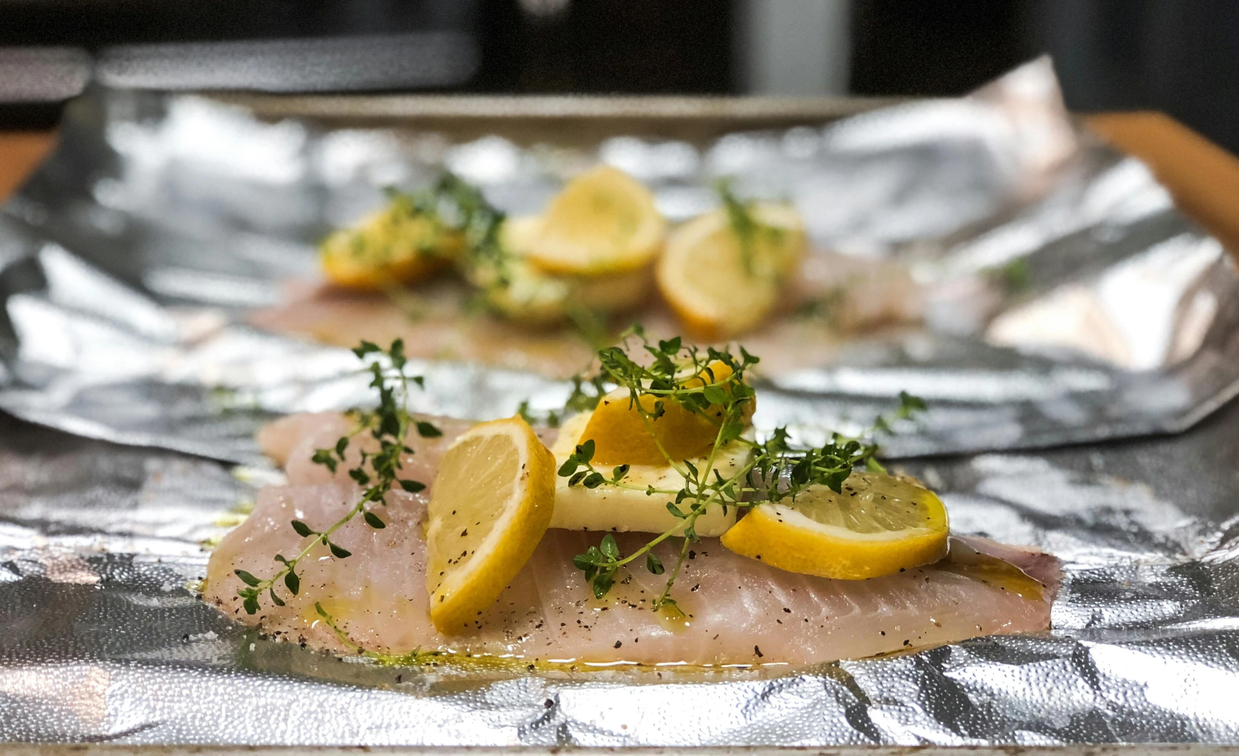 a sheet of foil sitting on top of a wooden table, by Josh Bayer, pexels, renaissance, lemon, fish, thumbnail, chicken