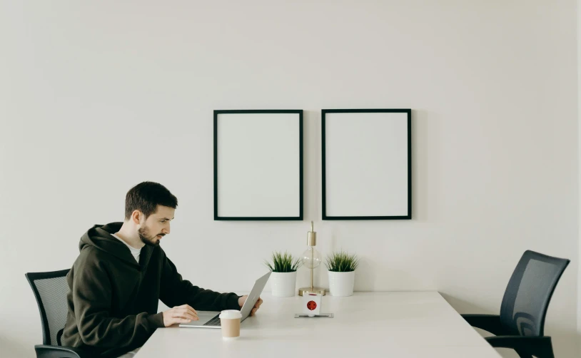 a man sitting at a table working on a laptop, a minimalist painting, trending on pexels, picture frames, white backdrop, small room, gif