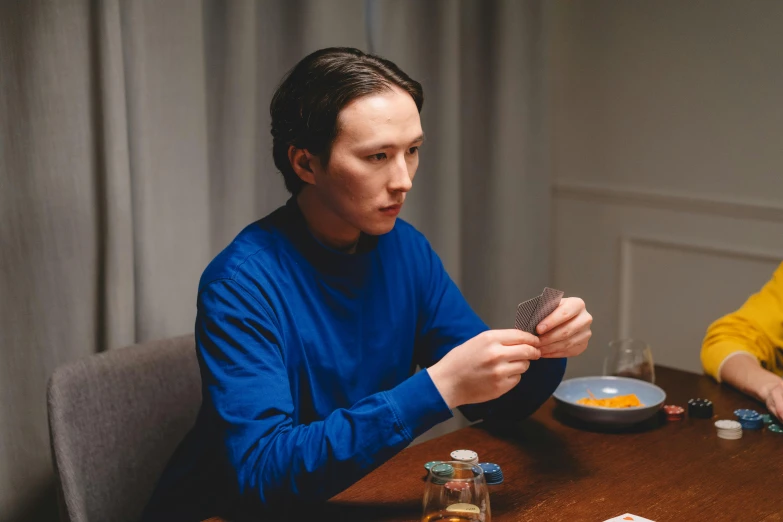 a couple of people that are sitting at a table, by Adam Marczyński, pexels contest winner, hyperrealism, cardistry, blue turtleneck, teenage boy, still from loki ( 2 0 2 1 )