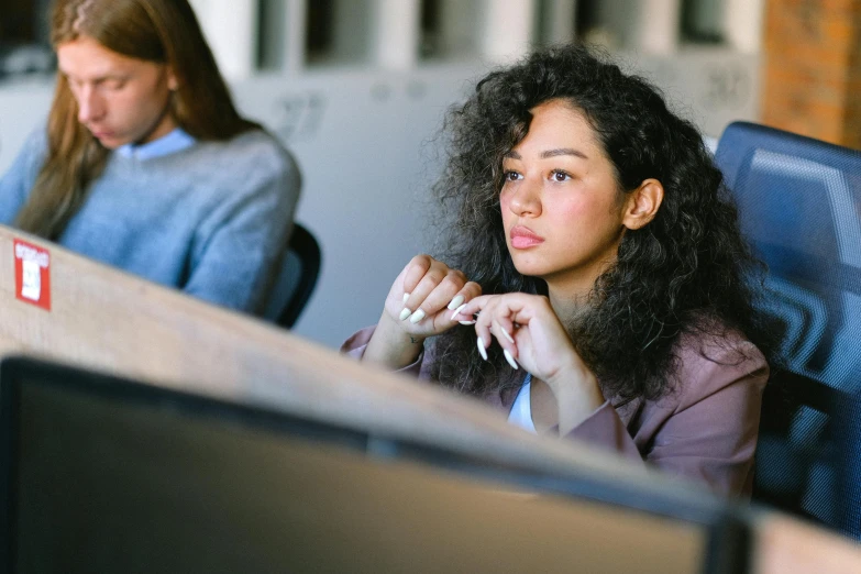 a woman sitting at a desk in front of a computer, trending on pexels, renaissance, sideways glance, two women, curly haired, sitting in the classroom