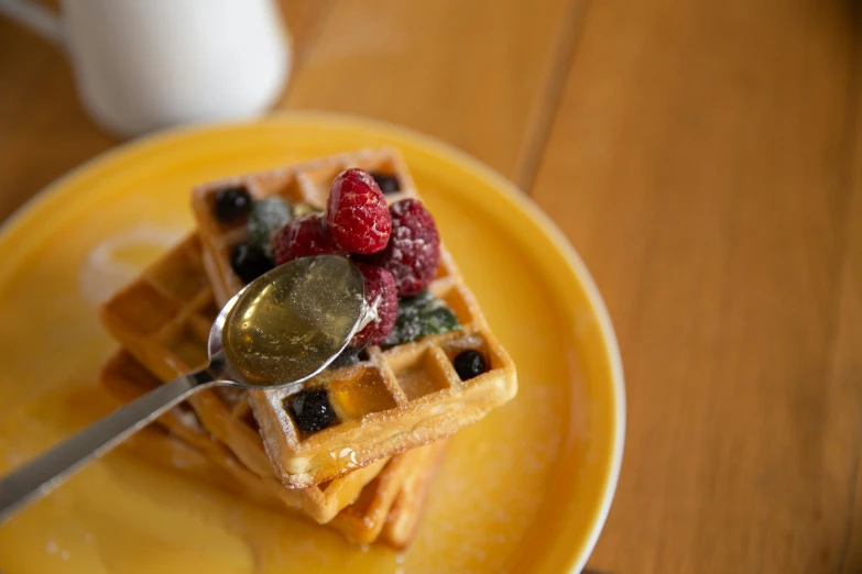 a yellow plate topped with waffles covered in fruit, a portrait, unsplash, hurufiyya, background image, spoon placed, mid shot photo, full daylight