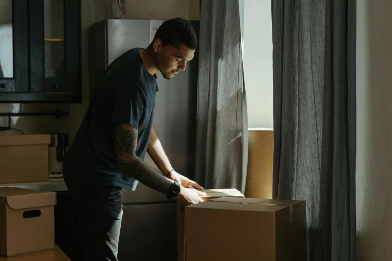 a man standing next to a stack of boxes, pexels contest winner, realism, window light, australian, bending down slightly, inspect in inventory image