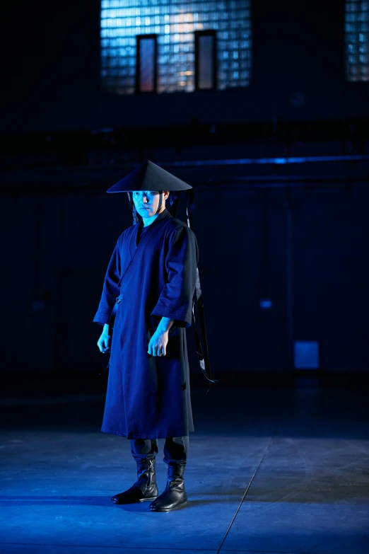 a man in a graduation gown standing in a dark room, inspired by Fu Baoshi, unsplash, conceptual art, hito steyerl, blue witch hat, performance, ( ( theatrical ) )