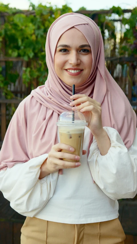 a woman wearing a hijab holding a drink, inspired by Muggur, shutterstock, sand color, 15081959 21121991 01012000 4k, milkshake, asian human