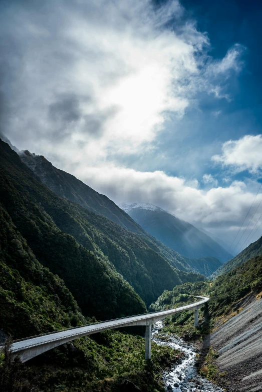 a river running through a valley next to a bridge, by Peter Churcher, unsplash, hurufiyya, covered in clouds, van, glacier, long street