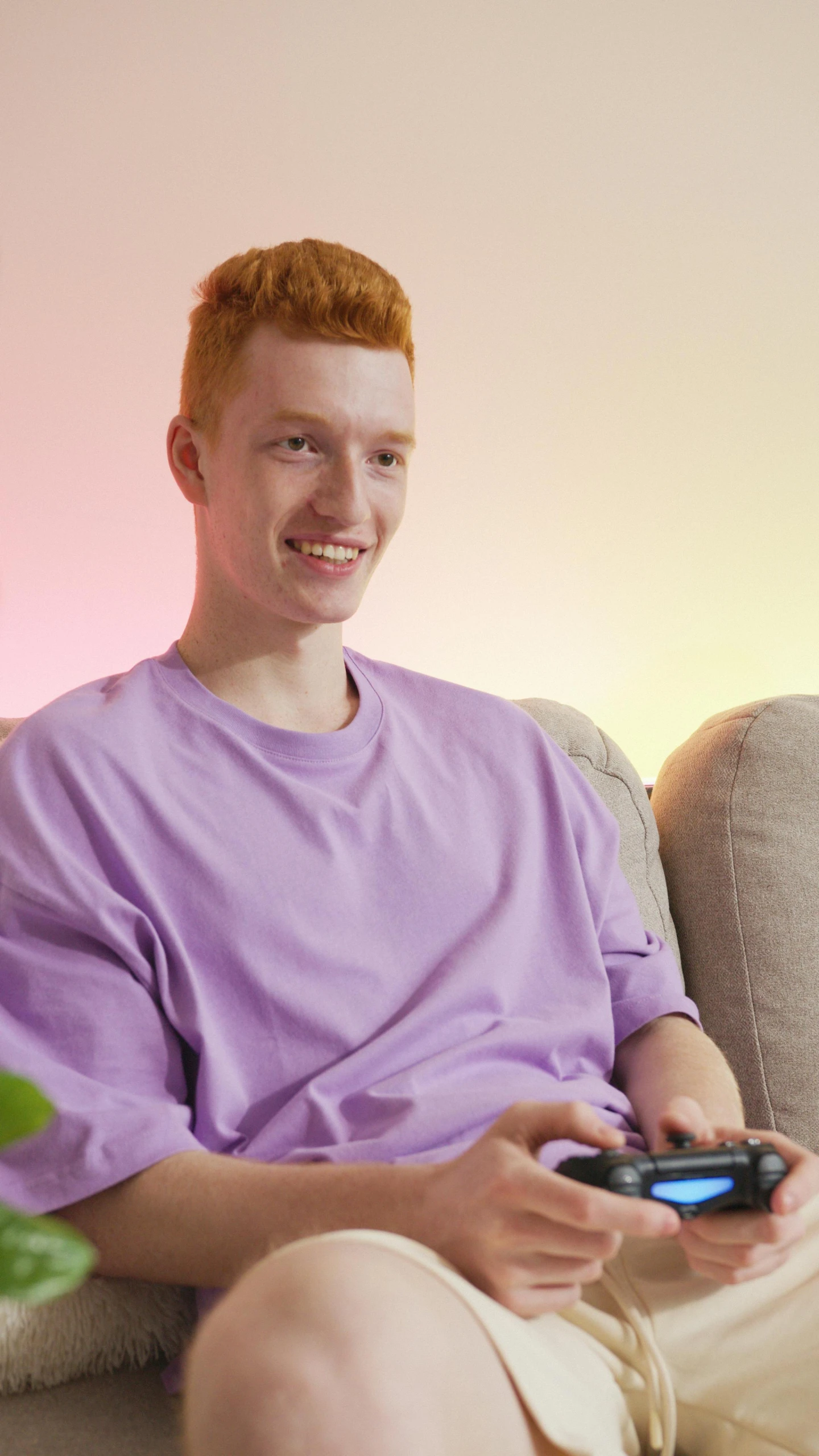 a man sitting on a couch holding a game controller, by Carey Morris, red haired teen boy, purple hue, promo photo, pastel clothing