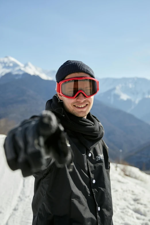 a man standing on top of a snow covered slope, wearing shiny black goggles, pointing at the camera, avatar image, sport