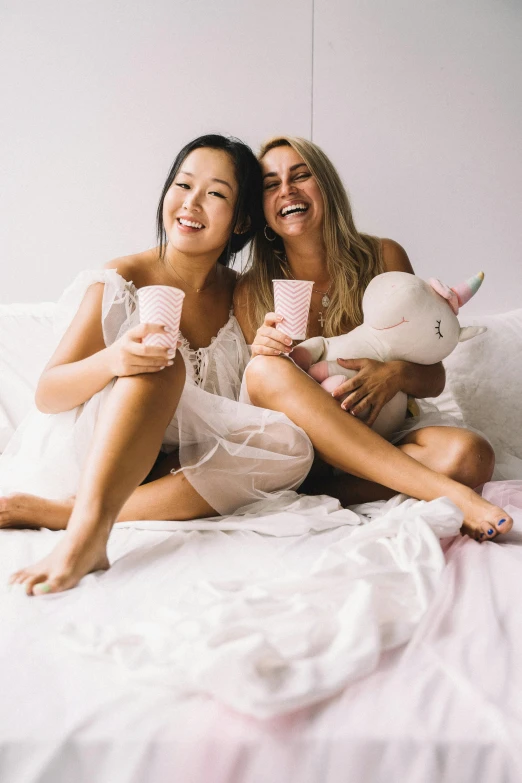 a couple of women sitting on top of a bed, inspired by Wang Duo, trending on unsplash, drink milkshakes together, jamie chung, unicorns, celebration of coffee products