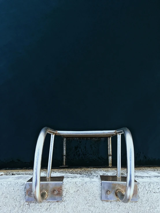 a metal bench sitting in front of a blue wall, inspired by Elsa Bleda, unsplash contest winner, dark blue water, reflected chrome, ignant, harbor