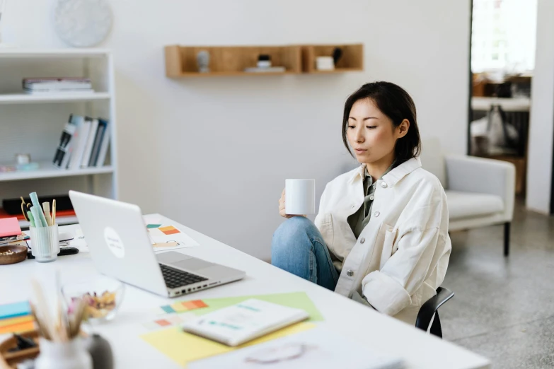 a woman sitting at a desk with a cup of coffee, trending on pexels, avatar image, japanese collection product, sitting in an empty white room, working on her laptop