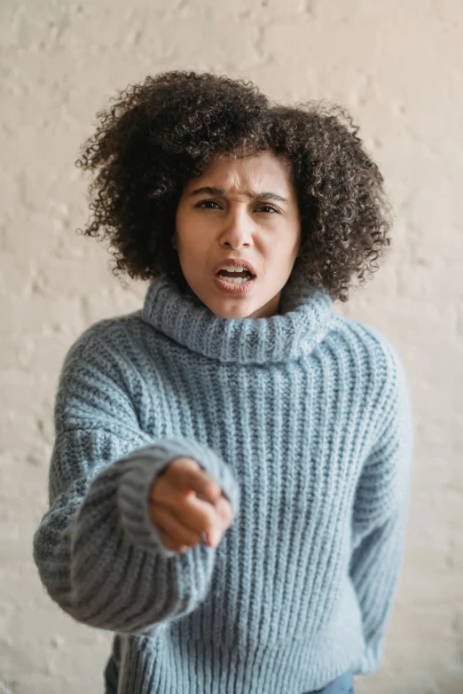 a woman in a blue sweater pointing at something, by Leo Michelson, trending on pexels, frown fashion model, mixed race, h3h3, scolding