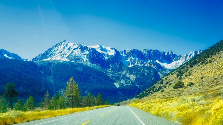 a car driving down a road with mountains in the background, an album cover, unsplash, mammoth, bright summer day, grand majestic mountains, chemistry