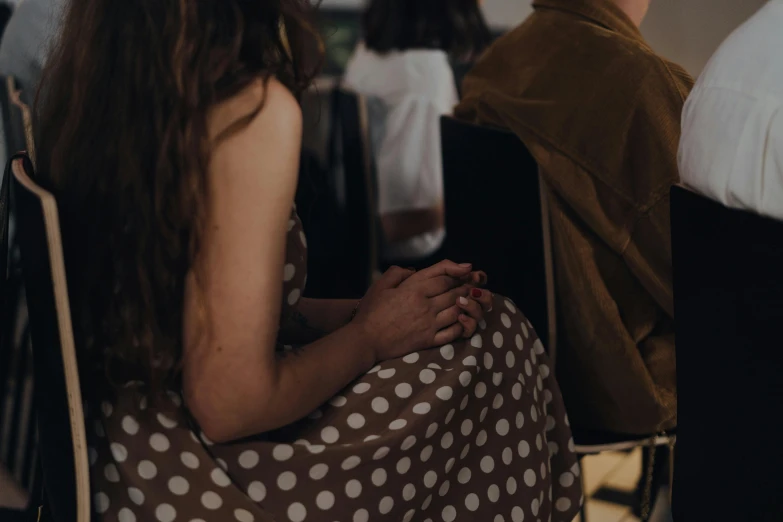 a group of people sitting next to each other, by Emma Andijewska, trending on pexels, girl in a dress, over the shoulder closeup, polka dot, holding hands