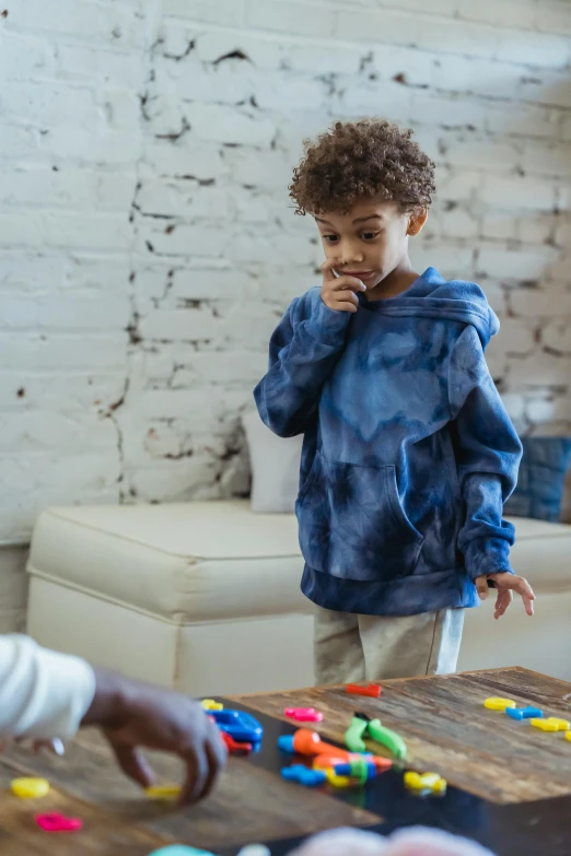 a little boy that is standing in front of a table, wearing a blue hoodie, kids playing, squish, multi chromatic