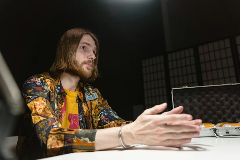 a man sitting at a table in front of a laptop computer, an album cover, unsplash, hyperrealism, mid long hair, cinematic outfit photo, holding a nintendo switch, linus from linustechtips