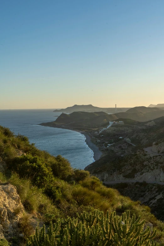 a man standing on top of a mountain next to the ocean, les nabis, a road leading to the lighthouse, costa blanca, which shows a beach at sunset, sparsely populated