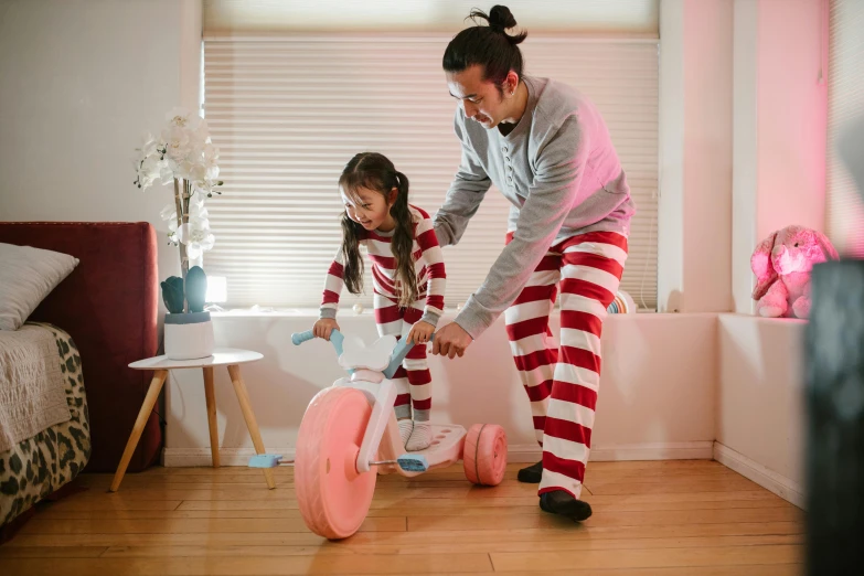 a woman teaching a young girl how to ride a tricycle, a picture, inspired by The Family Circus, pexels contest winner, wearing pajamas, asian man, fatherly, in australia