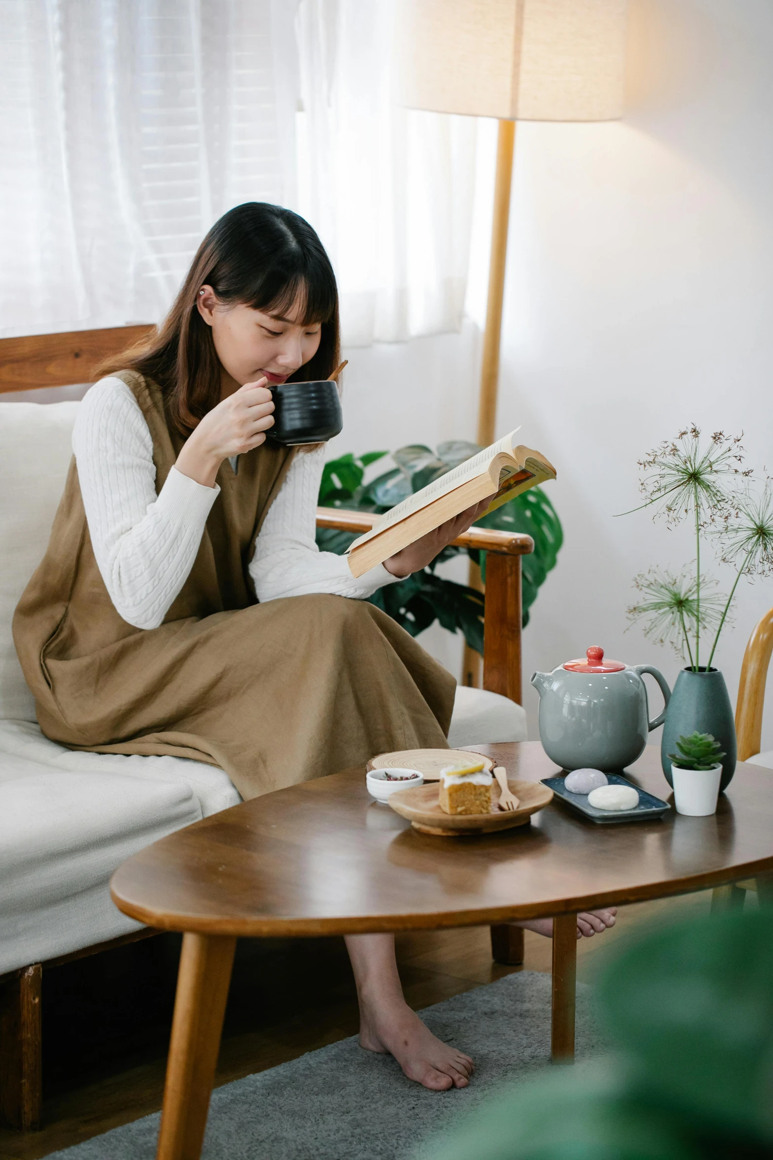 a woman sitting on a couch reading a book, by Sengai, trending on unsplash, mingei, sitting on a mocha-colored table, long dress with apron, casual clothing style, product introduction photo