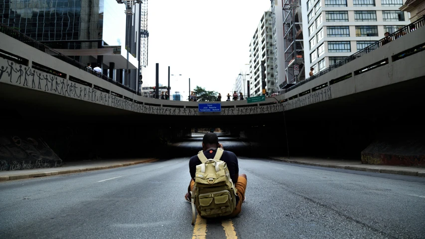 a man with a backpack sitting in the middle of a road, joel torres, underground, backpack, in sao paulo