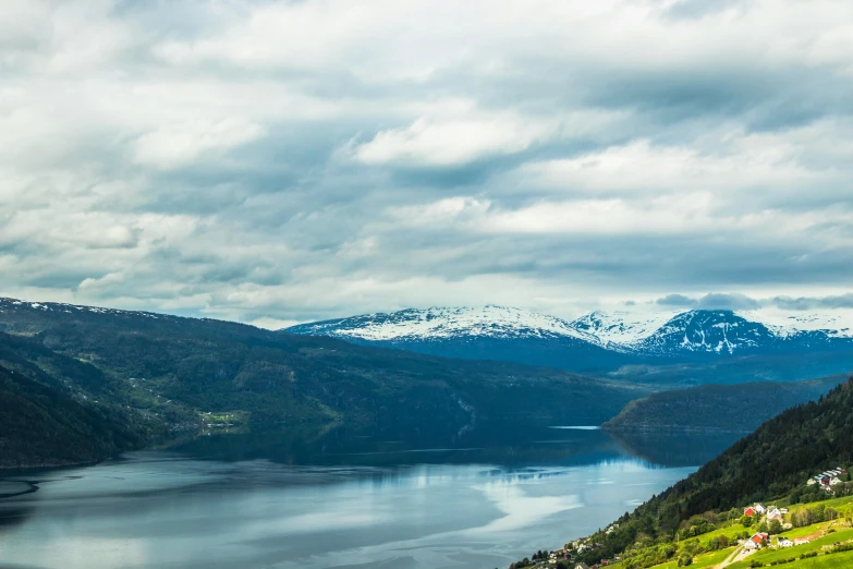 a large body of water sitting on top of a lush green hillside, by Jesper Knudsen, pexels contest winner, hurufiyya, snowy fjord, thumbnail, multiple stories, with mountains in background