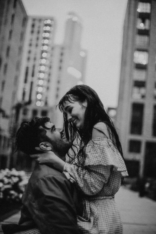 a couple standing next to each other in front of tall buildings, a black and white photo, by Emma Andijewska, pexels contest winner, jesus hugging a woman, attractive girl, happy cozy feelings, soaked