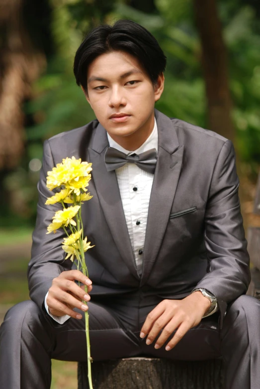 a man sitting on a tree stump holding a flower, by Basuki Abdullah, wearing tuxedo, silver and yellow color scheme, professional profile photo, he is about 20 years old | short