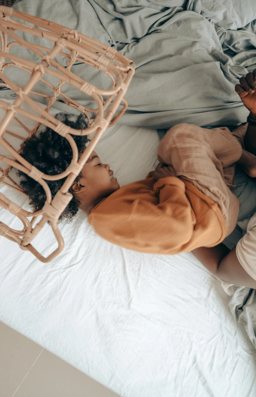 a couple of kids laying on top of a bed, by Daniel Lieske, trending on unsplash, light tan, intertwined full body view, with brown skin, with a kid