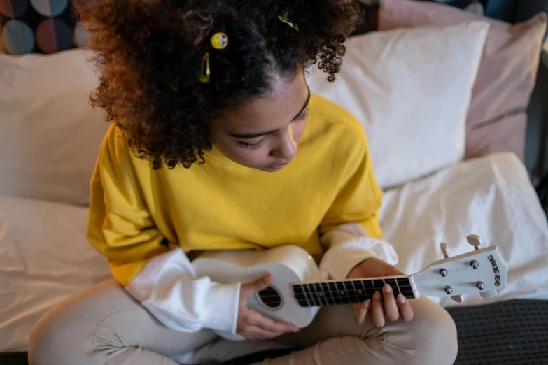 a young girl sitting on a bed playing a guitar, pexels contest winner, yellow clothes, connectivity, ukulele, black teenage girl