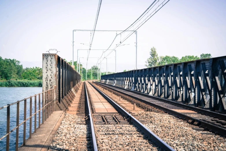 a train track next to a body of water, unsplash, figuration libre, electrical signals, metallic bridge, on a bright day, 15081959 21121991 01012000 4k