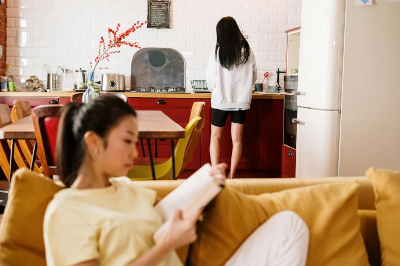 a woman sitting on a couch reading a book, by Julia Pishtar, pexels contest winner, in the kitchen, fiona staples and kinu nishimura, scarlet and yellow scheme, standing sideways