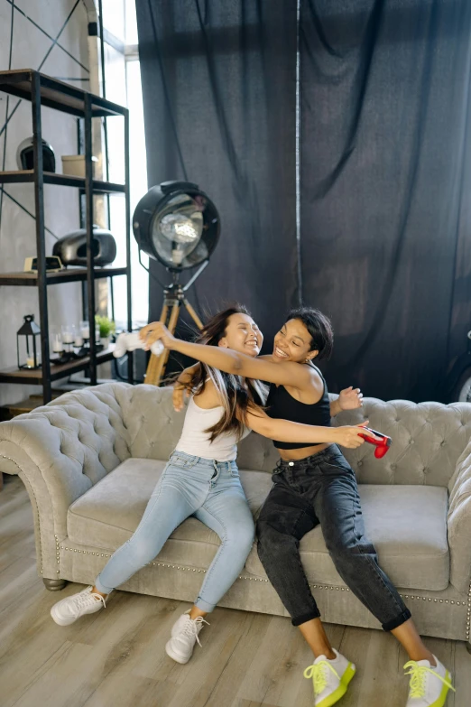 a couple of women sitting on top of a couch, a picture, pexels contest winner, waving at the camera, modeling studio, teenager hangout spot, black furniture