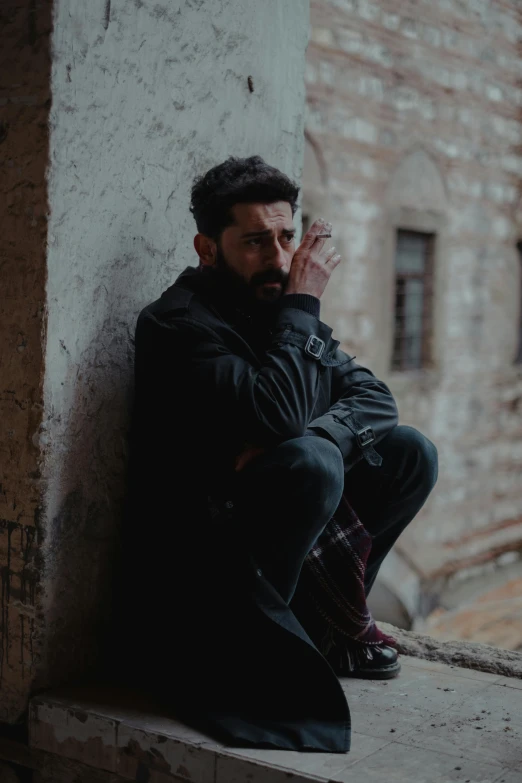 a man sitting on a ledge smoking a cigarette, pexels contest winner, renaissance, a portrait of rahul kohli, looking exhausted, man wearing a closed cowl, leaning against the wall