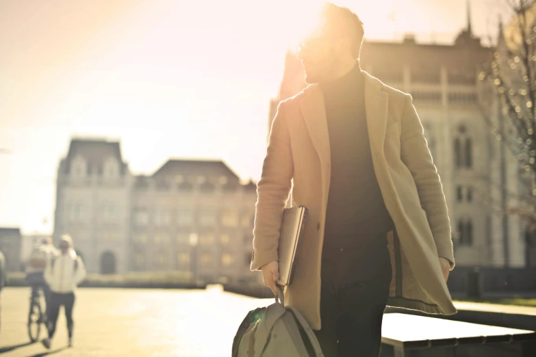 a man walking down a sidewalk carrying a bag, pexels contest winner, romanticism, sunflare, at the waterside, light brown trenchcoat, holding a briefcase