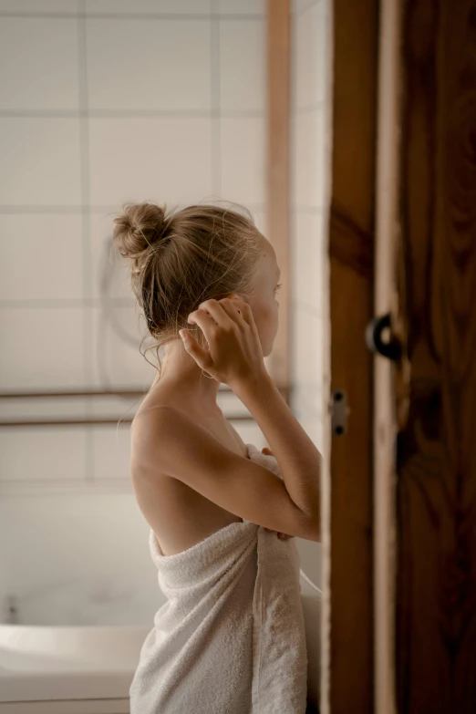 a woman standing in a bathroom with a towel over her head, inspired by Elsa Bleda, unsplash, renaissance, hair tied in a bun, waking up, young blonde woman, scratching head