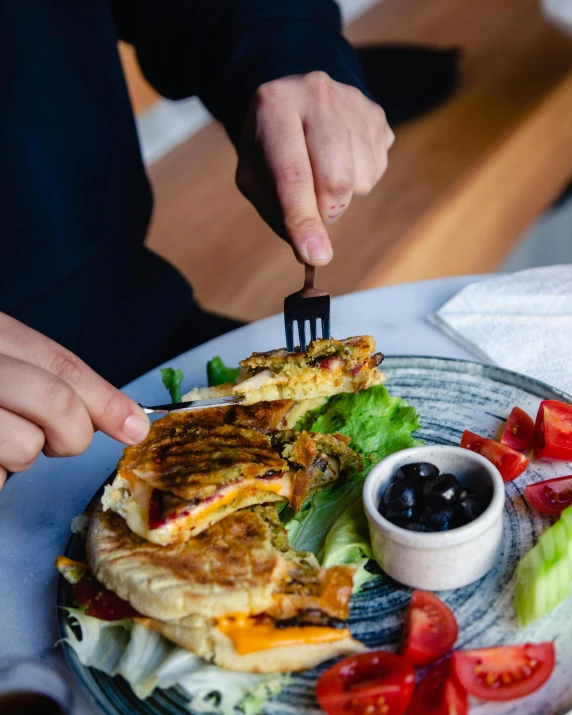 a person sitting at a table with a plate of food, hand holding a knife, panini, manuka, trending photo