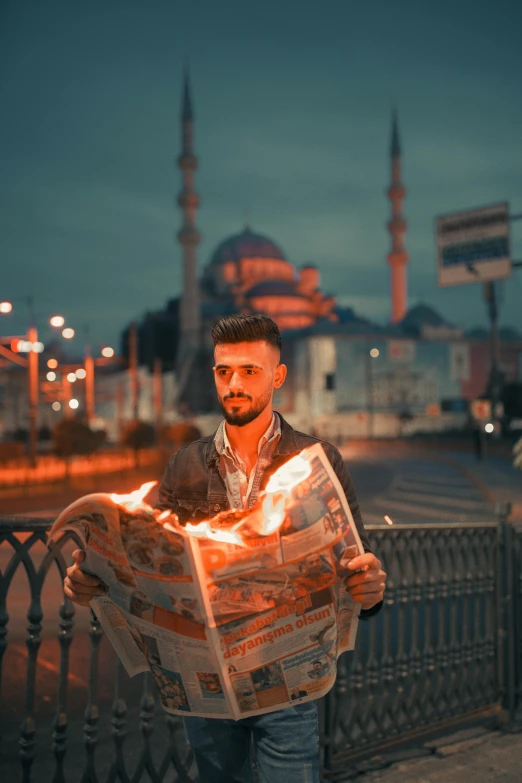 a man standing on a sidewalk reading a newspaper, an album cover, by Ismail Acar, pexels contest winner, all face covered with a fire, hero pose colorful city lighting, mosque, handsome girl