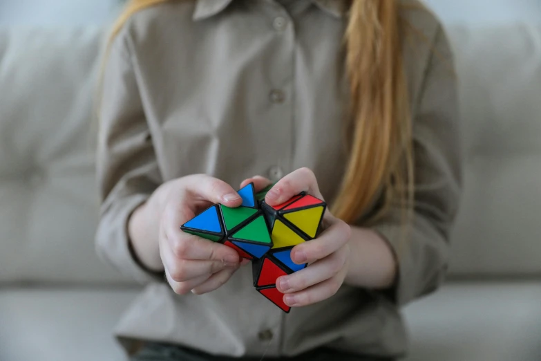 a little girl holding a rubik cube in her hands, a jigsaw puzzle, inspired by Ernő Rubik, trending on pexels, flat triangles, teenage girl, coloured, oversized shuriken