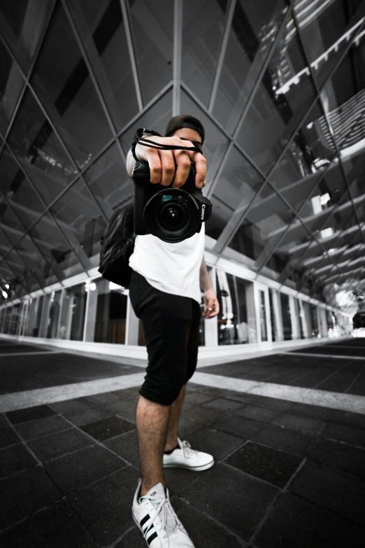 a man standing in front of a train holding a camera, by Robbie Trevino, dynamic perspective pose, sneaker photo, low quality photo, with a black background