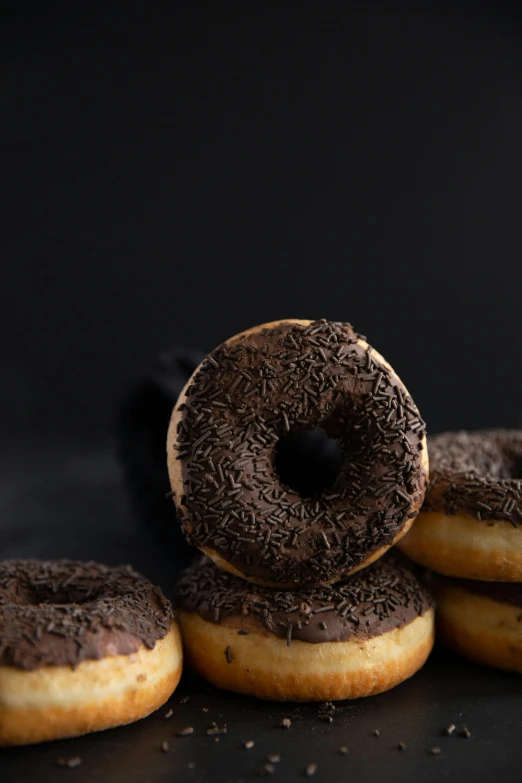 a pile of donuts with chocolate frosting and sprinkles, a portrait, unsplash, dark. no text, chilean, side profile shot, seeds