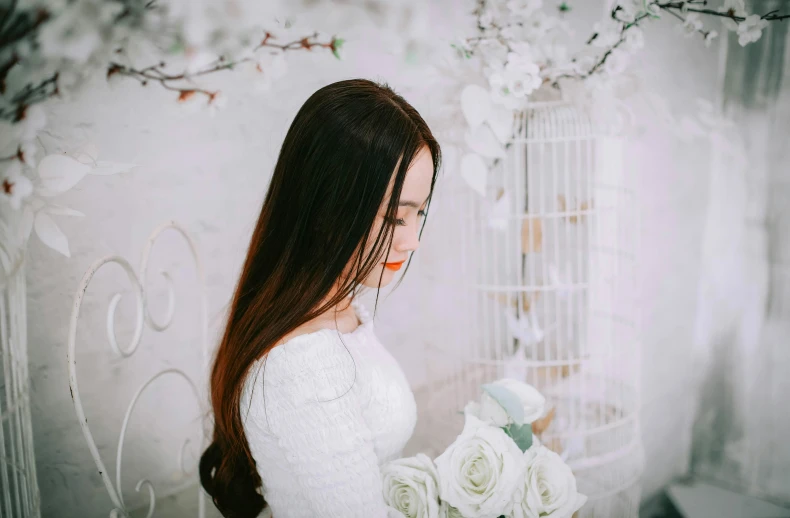 a woman in a white dress holding a bouquet of flowers, inspired by Kim Du-ryang, pexels contest winner, brown colored long hair, white room, girl with a birdcage on her head, gif