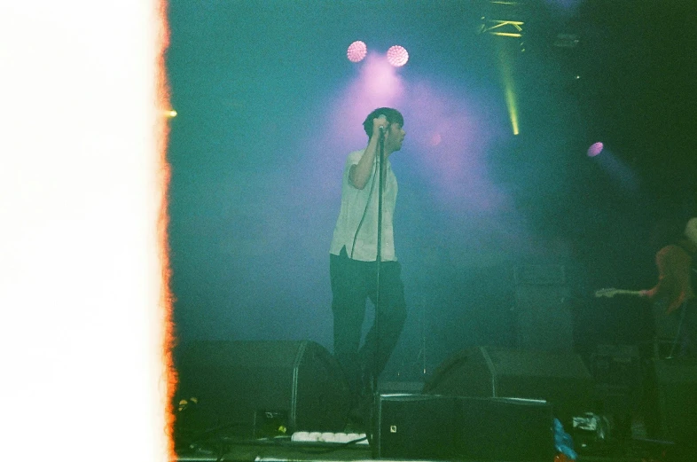 a man standing on top of a stage holding a microphone, a picture, unsplash, bauhaus, disposable colored camera, crystal castles, taken in the late 2000s, dim neon lights