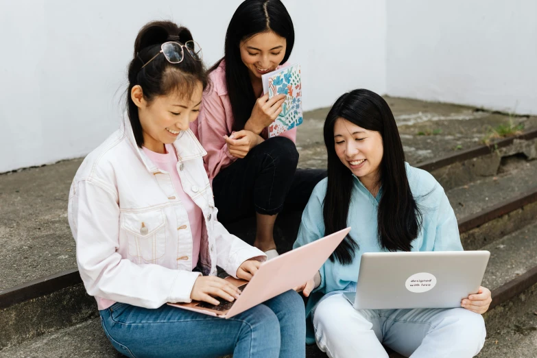 three women sitting on steps looking at a laptop, inspired by helen huang, trending on pexels, asian features, group of people, studious, multicoloured