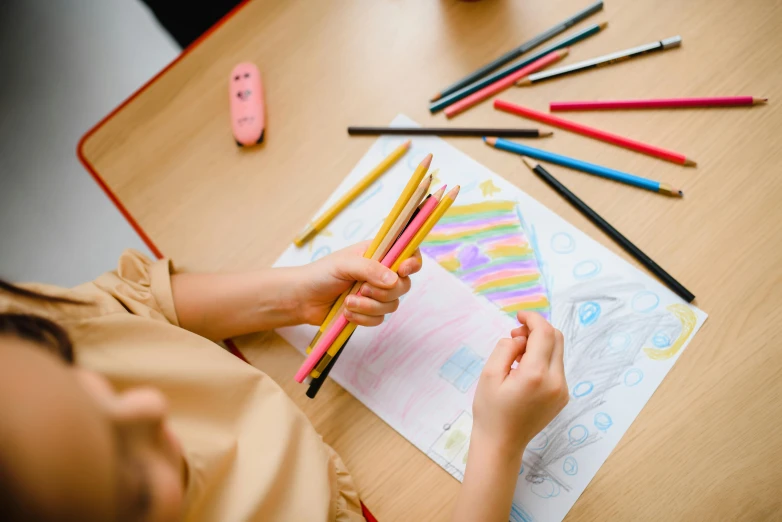 a child is drawing with colored pencils on a table, pexels contest winner, fan favorite, ornate designs on desk, private school, thumbnail