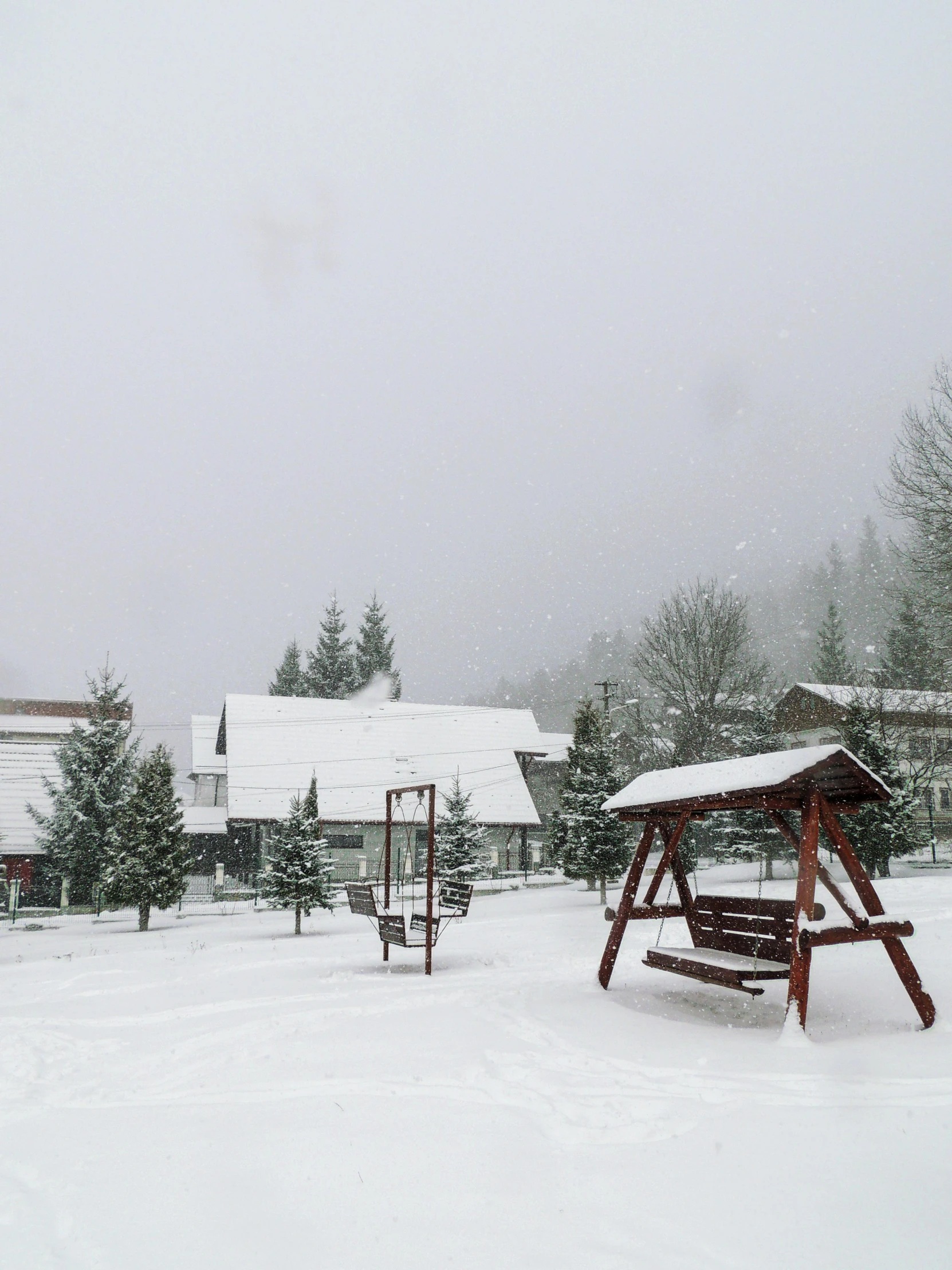 a wooden swing set sitting in the middle of a snow covered park, view of villages, foggy weather, daverapoza, 🌲🌌